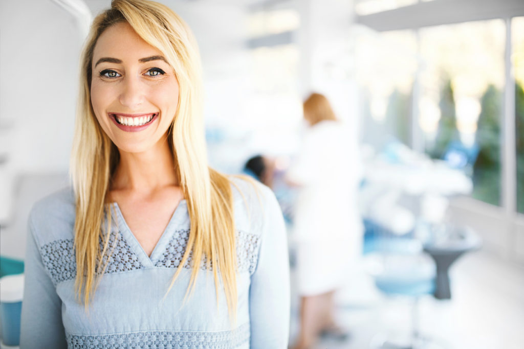 Conéctese Con Un Dentista De Unitedhealthcare 4 Young Female Patient Smiling And Looking At Camera In A Dental Office. Shes Satisfied With Results. Focus On Foreground.